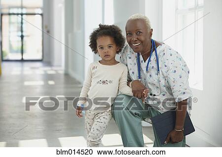 Stock Image - Black nurse standing in corridor with girl. Fotosearch