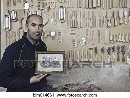 Stock Image - Carpenter holding old photograph in workshop. Fotosearch