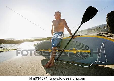 Stock Image - Caucasian man leaning on paddleboard. Fotosearch