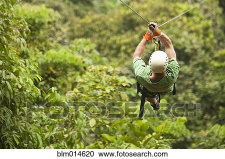 Stock Image - Caucasian man on zip line in forest. Fotosearch