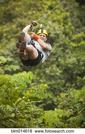 Stock Photo - Caucasian man on zip line in forest. Fotosearch