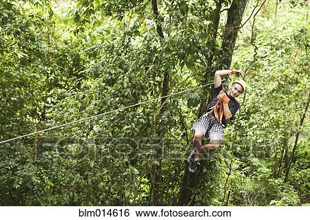 Stock Photograph - Caucasian man on zip line in forest. Fotosearch