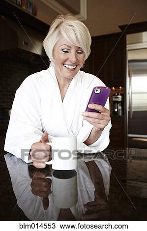Stock Image - Caucasian woman in robe using cell phone. Fotosearch