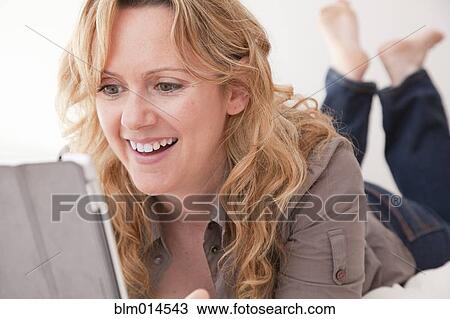 Caucasian woman laying on bed using digital tablet View Large Photo Image Stock Image - Caucasian woman laying on bed using digital tablet. Fotosearch