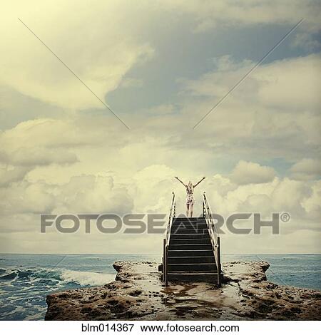 Stock Photo - Caucasian woman on stairs on rocks next to ocean. Fotosearch