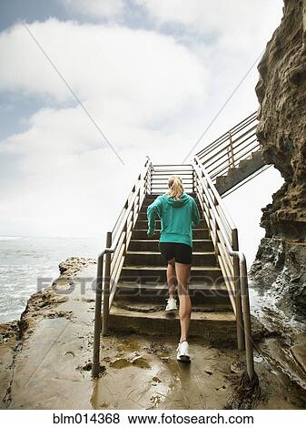 Stock Photo - Caucasian woman running up stairs next to ocean. Fotosearch