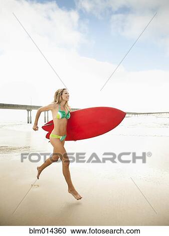 Stock Image - Caucasian woman running with surfboard. Fotosearch