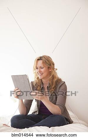 Caucasian woman sitting on bed using digital tablet View Large Photo Image Picture - Caucasian woman sitting on bed using digital tablet. Fotosearch