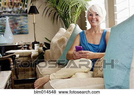 Stock Photo - Caucasian woman sitting sofa text messaging on cell phone. Fotosearch