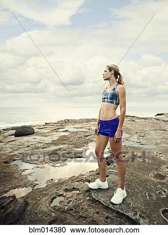Stock Image - Caucasian woman standing on rocks near beach. Fotosearch