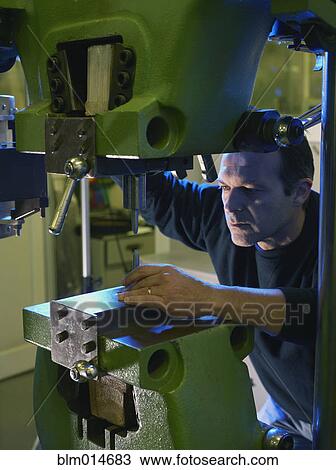 Stock Image - Caucasian worker using industrial drill. Fotosearch