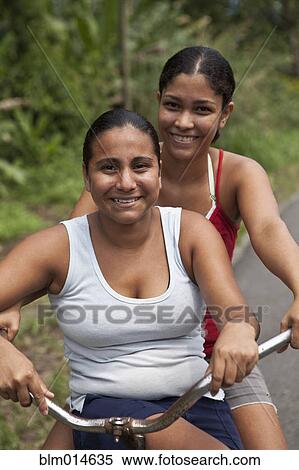 Stock Photography - Hispanic friends riding bicycle together. Fotosearch