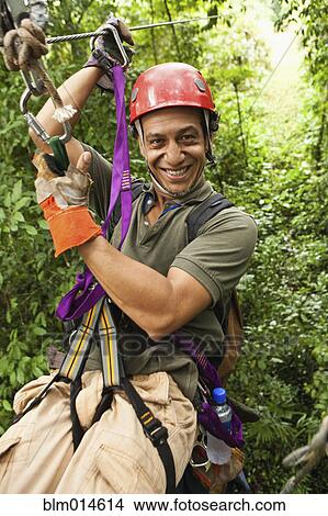 Picture - Hispanic man on zip line in forest. Fotosearch
