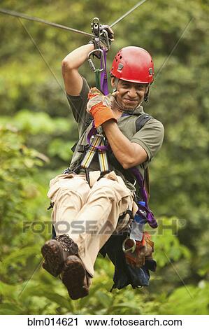 Stock Image - Hispanic man on zip line in forest. Fotosearch