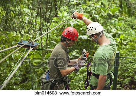 Stock Photo - Man being helped onto zip line. Fotosearch