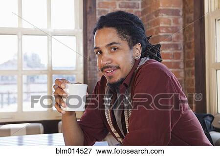 Stock Photo - Mixed race man drinking coffee in coffee shop. Fotosearch