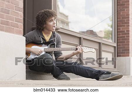 Stock Image - Mixed race teenager playing electric guitar and singing. Fotosearch