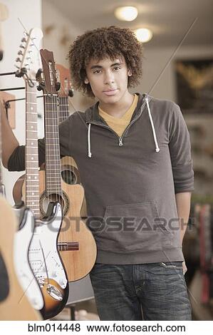 Stock Photo - Mixed race teenager standing with guitars in music store. Fotosearch