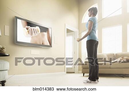 Stock Image - Mixed race woman watching exercise program on television. Fotosearch