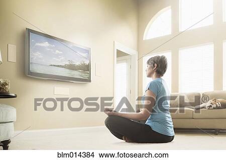 Picture - Mixed race woman watching meditation program on television. Fotosearch