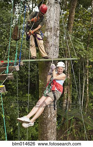 Stock Photograph - Woman being helped onto zip line in forest. Fotosearch