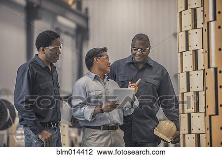 Stock Image - Workers looking at equipment in factory. Fotosearch