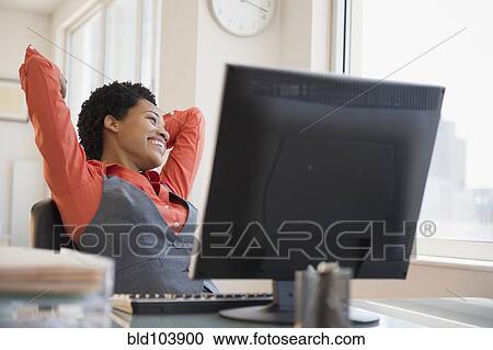 Stock Image - African American businesswoman relaxing at desk. Fotosearch