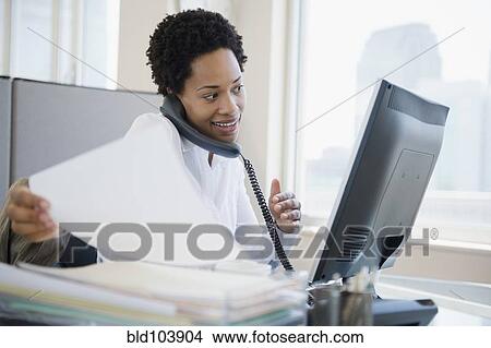 Picture - African American businesswoman using computer and talking on telephone. Fotosearch