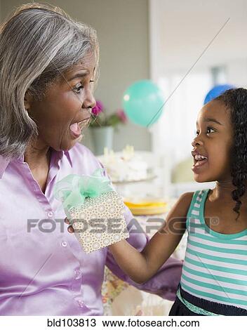 Stock Image - African American girl giving grandmother a gift. Fotosearch