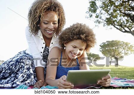 Stock Image - African American mother and daughter using digital tablet in park. Fotosearch