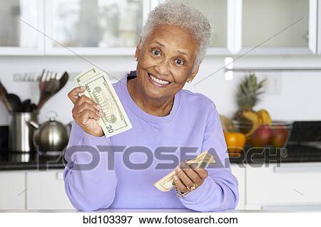 Stock Photo - African American woman counting money in kitchen. Fotosearch