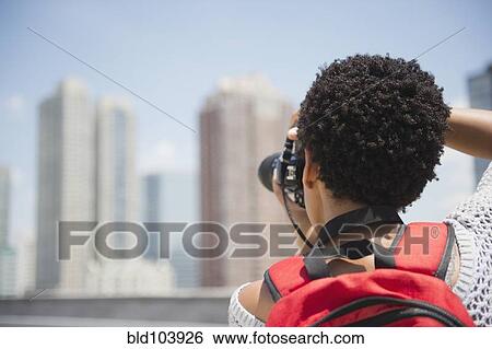 Stock Photograph - African American woman taking photographs of cityscape. Fotosearch