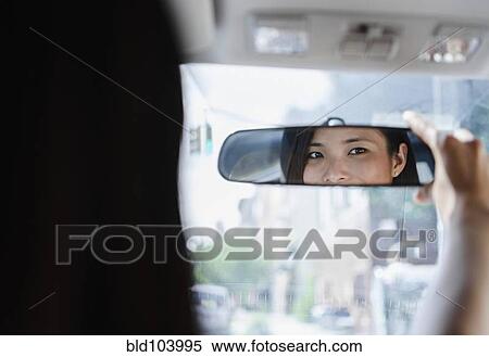 Stock Photography - Asian woman adjusting rear-view mirror. Fotosearch