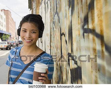 Asian woman listening to headphones and drinking coffee View Large Photo Image Stock Photo - Asian woman listening to headphones and drinking coffee. Fotosearch