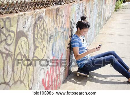 Stock Photography - Asian woman sitting on skateboard using cell phone. Fotosearch