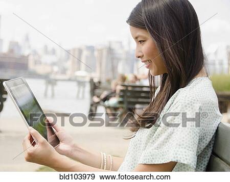 Stock Photo - Asian woman using digital tablet outdoors. Fotosearch