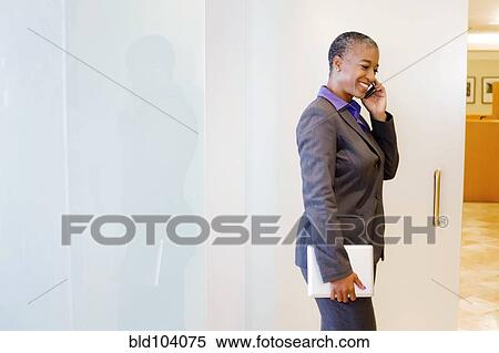 Stock Photography - Black businesswoman holding digital tablet and using cell phone. Fotosearch
