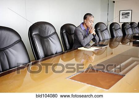 Stock Image - Black businesswoman sitting in empty conference room. Fotosearch