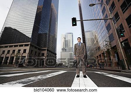 Stock Image - Businessman standing in urban crosswalk. Fotosearch