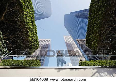 Stock Photo - Businessman standing on balcony text messaging on cell phone. Fotosearch