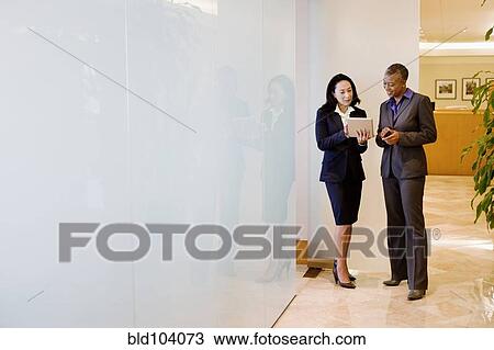 Stock Image - Businesswomen using digital tablet in office corridor. Fotosearch