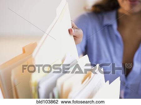 Stock Image - Cape Verdean woman picking up file folder. Fotosearch