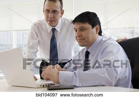Stock Photo - Hispanic businessman looking at laptop together. Fotosearch