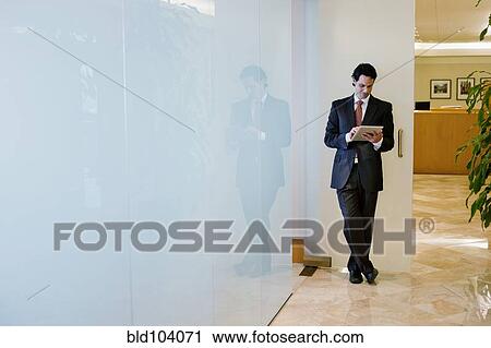 Stock Image - Hispanic businessman using digital tablet in office corridor. Fotosearch
