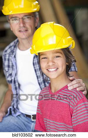 Stock Image - Hispanic carpenter and son in hard hats. Fotosearch