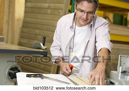 Stock Image - Hispanic carpenter measuring wood in workshop. Fotosearch