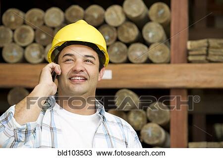Stock Image - Hispanic carpenter talking on cell phone. Fotosearch