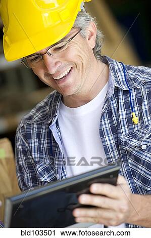 Stock Image - Hispanic carpenter using digital tablet. Fotosearch
