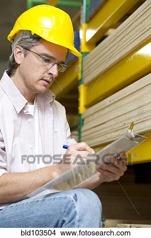 Picture - Hispanic carpenter writing on clipboard. Fotosearch