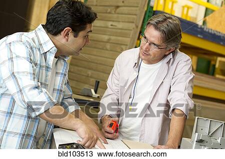 Stock Image - Hispanic carpenters talking in workshop. Fotosearch